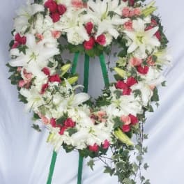 Heart-shaped floral wreath with white lilies and pink roses on a stand