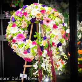 Large floral wreath on an easel with pink, white, peach, and purple flowers.