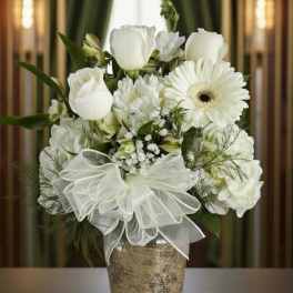White roses and gerbera daisies in a glass vase with a white bow