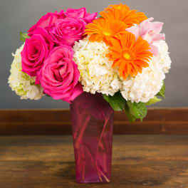 Pink roses and orange gerbera daisies in a tall magenta vase