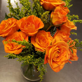 Orange roses arranged in a clear glass vase with green filler flowers