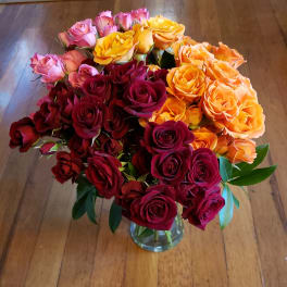 Bouquet of red, pink, orange, and yellow roses in a clear glass vase