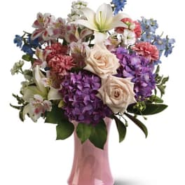 Mixed bouquet of roses, lilies, hydrangeas, and carnations in a pink vase