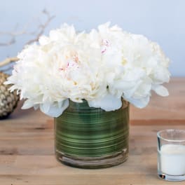 White peonies in a green glass vase on a table