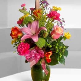 Colorful mixed bouquet in a green glass vase with pink lilies and roses