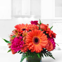 Bright orange and pink mixed bouquet in a square glass vase