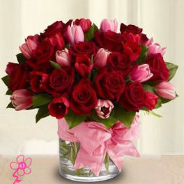 Bouquet of red roses and pink tulips in a glass vase with a pink ribbon