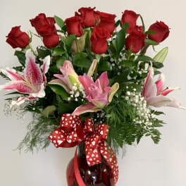 Bouquet of red roses and pink lilies in a red glass vase with a heart ribbon