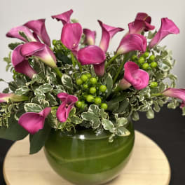 Pink calla lilies arranged in a green vase with variegated foliage