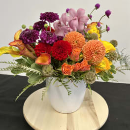 Colorful mixed bouquet in a white vase with dahlias, orchids, roses, and calla lilies