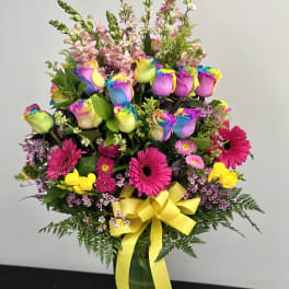 Colorful bouquet of rainbow roses and pink flowers in a glass vase with a yellow ribbon