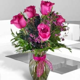 Pink roses arranged in a glass vase with a ribbon