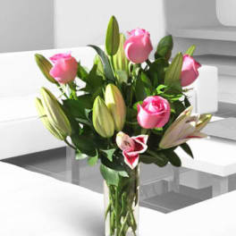Pink roses and lily buds arranged in a clear glass vase