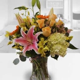 Mixed bouquet with pink lilies, peach roses, and hydrangeas in a glass vase