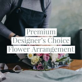 Florist in an apron arranging a pastel pink and white rose bouquet on a wooden table