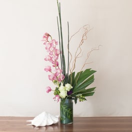 Tall modern arrangement with pink orchids and white roses in a clear cylinder vase