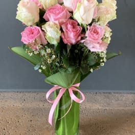 Bouquet of pink and white roses in a tall glass vase with a pink ribbon