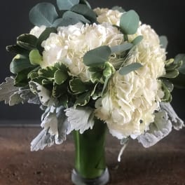 White hydrangea bouquet in a green glass vase with eucalyptus