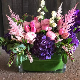 Pink and purple floral arrangement in a green glass vase