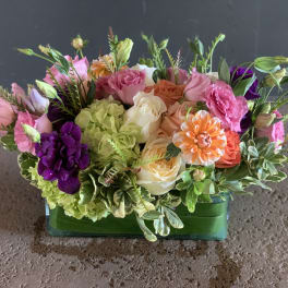 Mixed bouquet in a green glass vase with pink, purple, peach, and white flowers