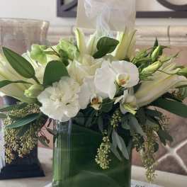 White floral arrangement in a glass vase with orchids and lilies