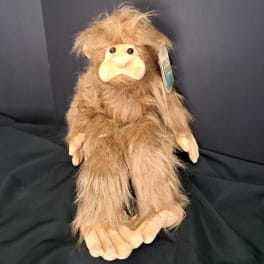 Plush monkey toy with shaggy brown fur and a pale face on a dark fabric background