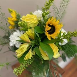 Bouquet of yellow roses, sunflowers, and white blooms in a glass vase