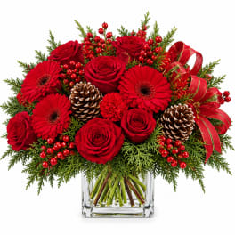 Red roses and gerbera daisies in a glass vase with pinecones and ribbon