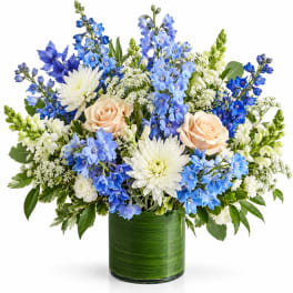 Blue and white floral arrangement with peach roses in a green glass vase