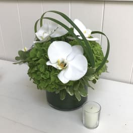 White orchids arranged in a green container with a small candle beside it
