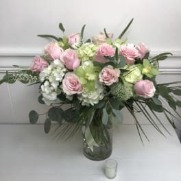 Large arrangement of pink roses, green orchids, and white hydrangeas in a clear glass vase with a small votive candle.