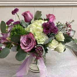 Pink and white floral arrangement in a clear glass vase with a lavender ribbon