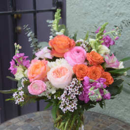 Mixed bouquet of pink and orange roses and other flowers in a clear glass vase