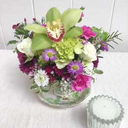 Mixed bouquet with green orchids, white roses, and pink flowers in a teacup-style vase