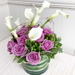 Purple roses and white calla lilies in a striped ceramic vase