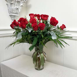 Red roses arranged in a clear glass vase with greenery
