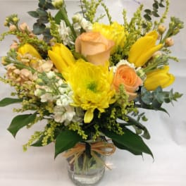 Yellow and peach flower arrangement with roses and tulips in a clear glass jar tied with raffia