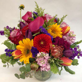 Mixed bouquet with sunflowers, tulips, roses, and calla lilies in a glass vase