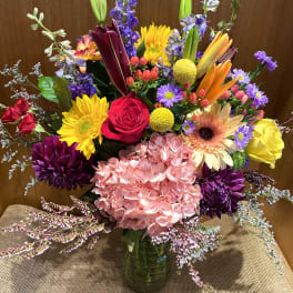 Colorful mixed bouquet in a glass vase with roses, lilies, and hydrangea