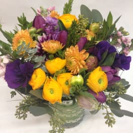 Round arrangement of yellow and purple flowers in a green glass vase