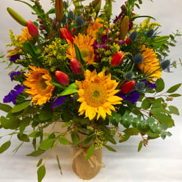 Bouquet of sunflowers, tulips, and purple accents in a burlap-wrapped vase