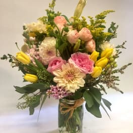 Mixed bouquet of pink roses, cream dahlias, and yellow tulips arranged in a glass mason jar vase.