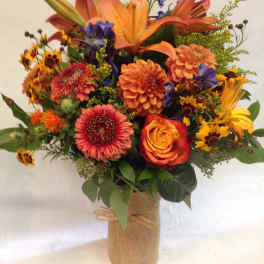 Colorful bouquet of lilies, roses, and daisies in a burlap-wrapped vase