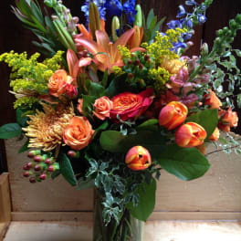Mixed bouquet of orange, blue, and yellow flowers in a glass vase