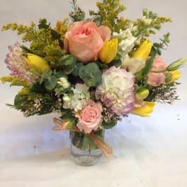 Pastel bouquet of pink roses, yellow tulips, and white blooms arranged in a mason jar vase.
