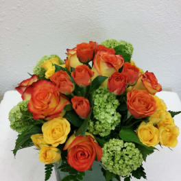 Bouquet of orange and yellow roses with green hydrangeas in a square glass vase