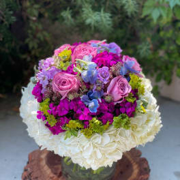 Round bouquet of pink roses, hydrangeas, and purple flowers in a glass vase