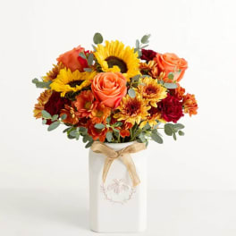 Bouquet of sunflowers, roses, and mums in a white vase with a ribbon