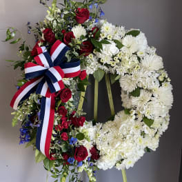 Two floral wreaths on stands, one red white and blue with roses and one white with chrysanthemums