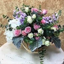 Bouquet of pink and white roses with lavender flowers in a round container